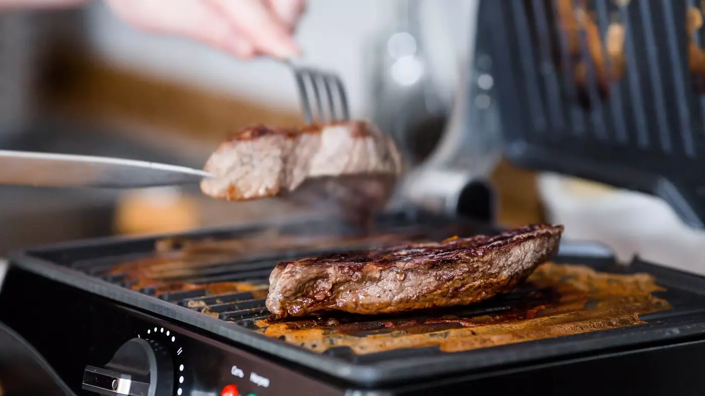 Eine Person grillt Fleisch auf einem Kontaktgrill.