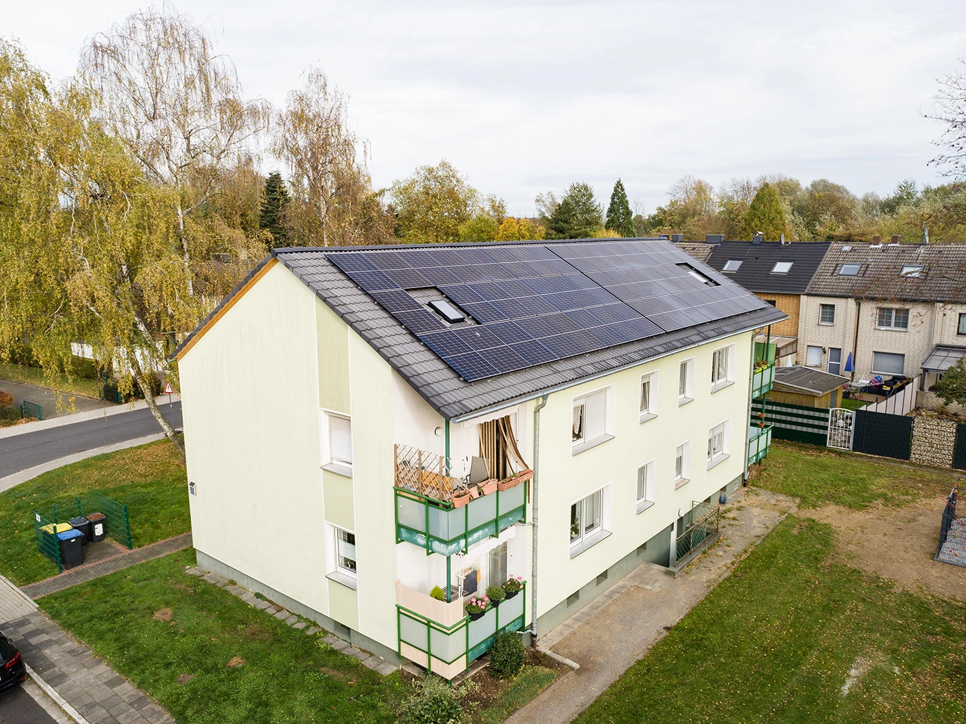 Weißes Mehrfamilienhaus von oben. Auf dem Dach befinden sich PV-Anlagen