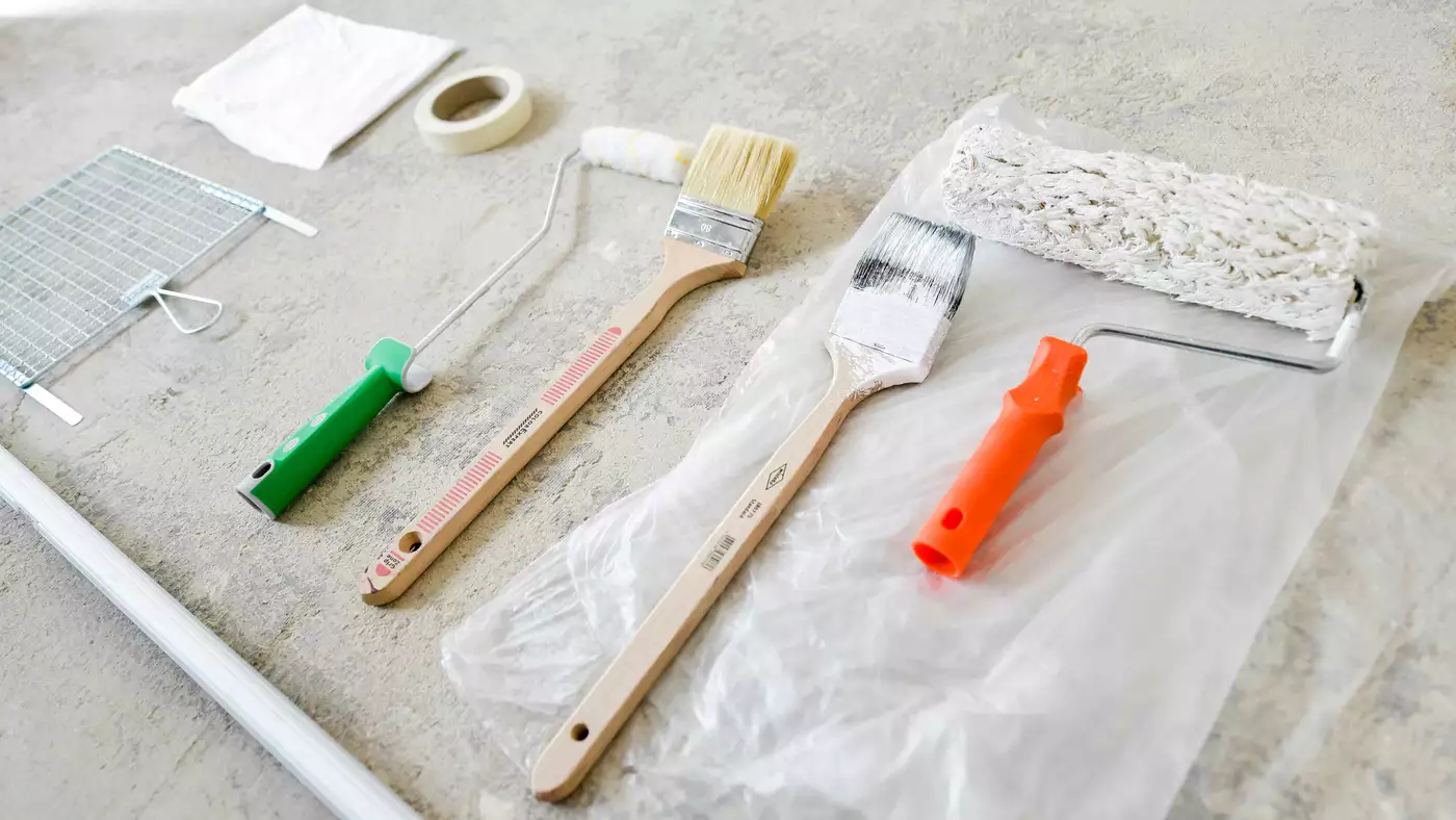 Utensilien die man für das Renovieren einer Wohnung benötigt. Zu sehen sind Pinsel und Farbrollen in unterschiedlichen Größen, gelbes Klebeband, um die Räume abzukleben sowie Abdeckfolie.