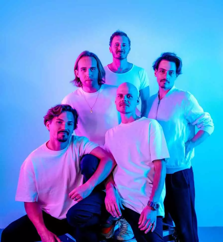 Die fünf Mitglieder der Band Cat Ballou blicken frontal in die Kamera. Sie sind vor einem hellen Hintergrund abgebildet und tragen alle weiße T-Shirts und dunkle Hosen. Ihre Gesichter werden mit rotem Licht angestrahlt, so dass eine Gesichtshälfte in rotes Licht getaucht ist.